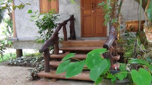 Una escalera de madera rústica que conduce a una puerta, rodeada de abundante vegetación y plantas en macetas.