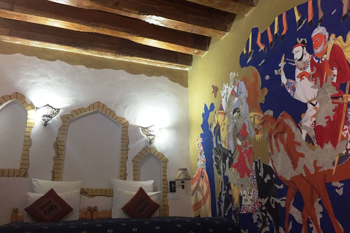 Une pièce avec un lit, un mur orné d’une fresque colorée et un plafond en bois.