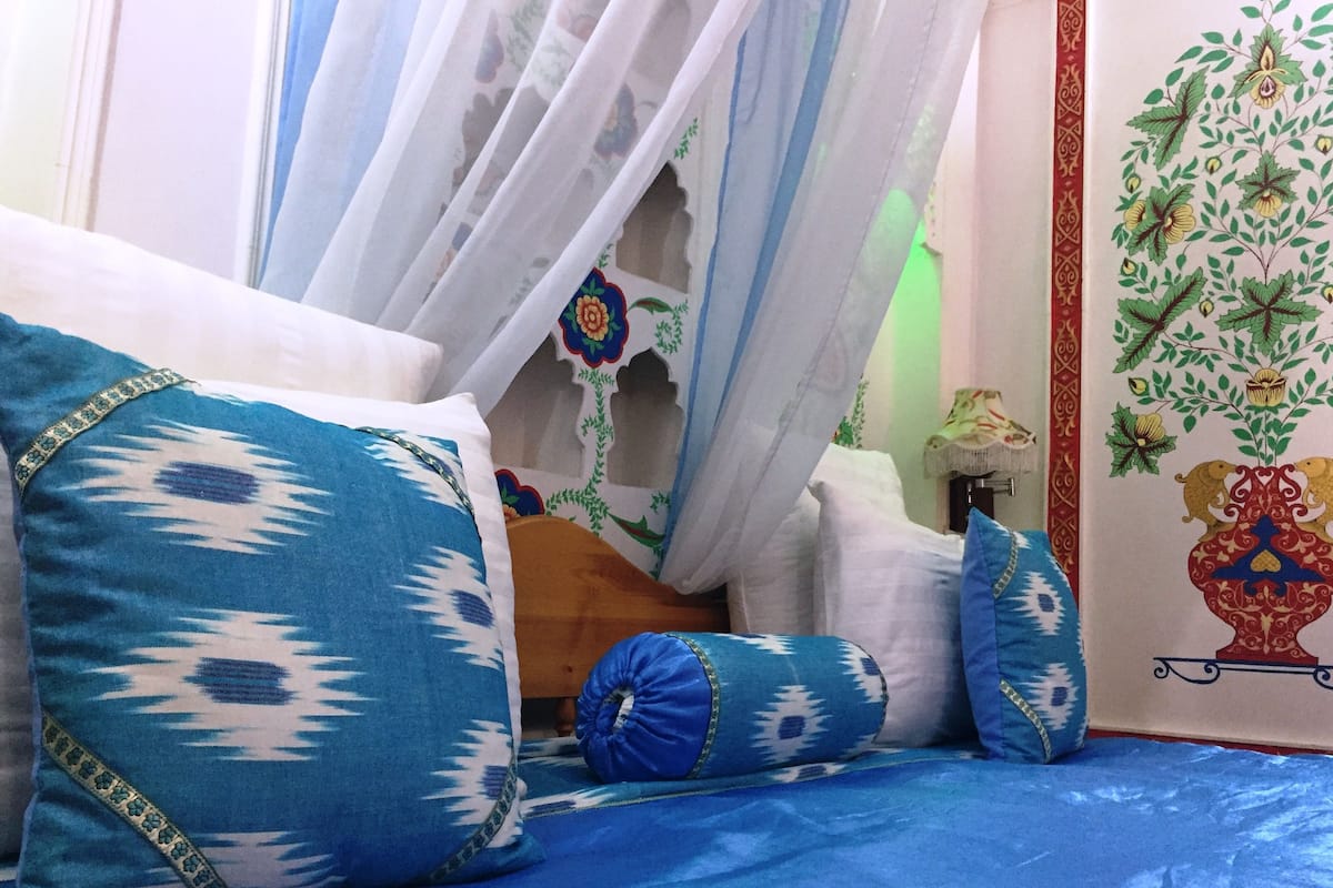 Un lit avec des oreillers à motifs bleus et blancs, un baldaquin et un mur recouvert d’un papier peint à motifs floraux.