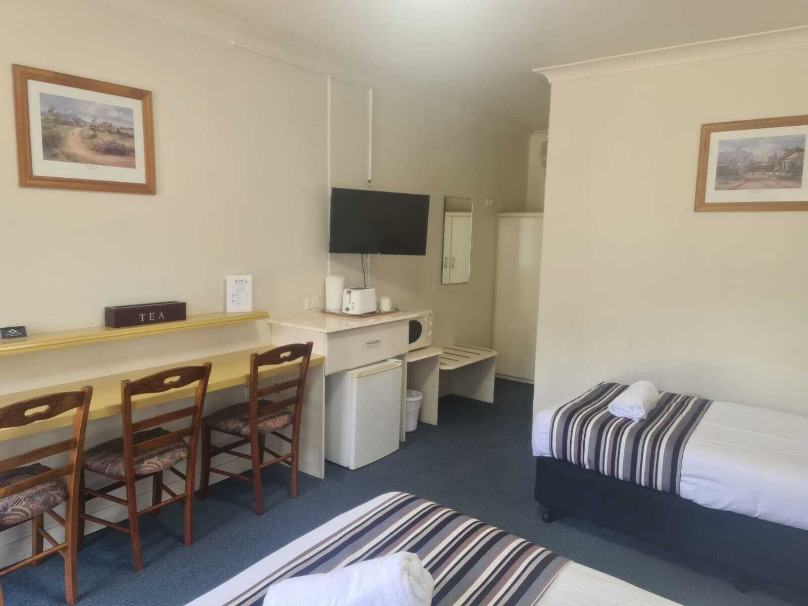 A hotel room with a desk, two single beds, a TV, a microwave, and a small refrigerator.