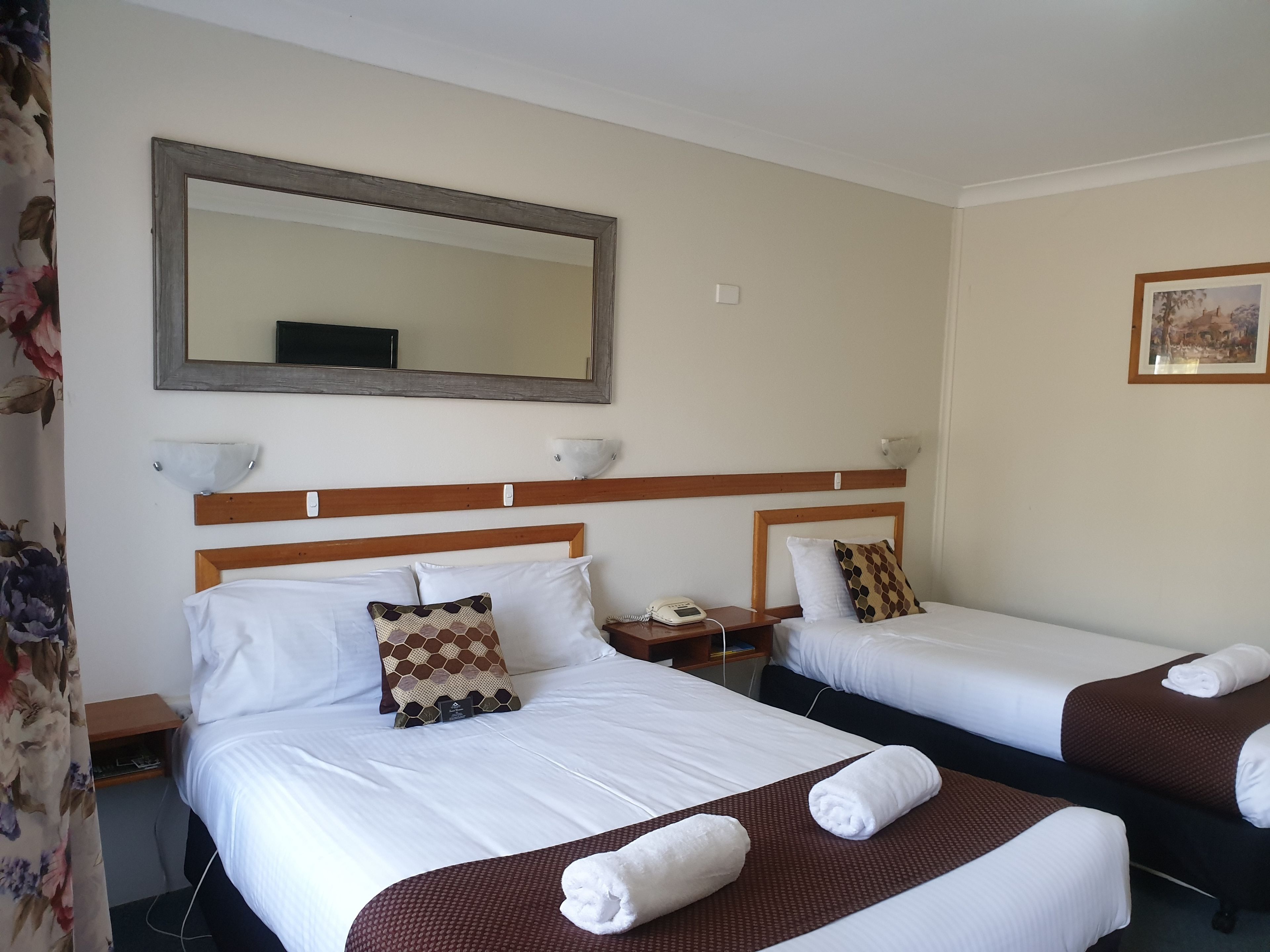 Een hotelkamer met twee bedden, een grote spiegel, nachtkastjes en een schilderij aan de muur.