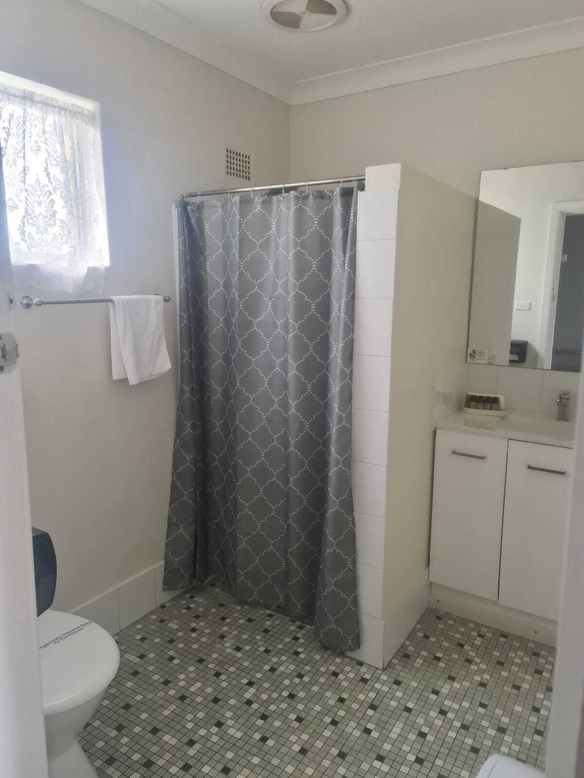 A bathroom with a shower curtain, a toilet, a sink with a mirror, and tiled flooring.