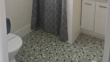 A bathroom with a shower curtain, a toilet, a sink with a mirror, and tiled flooring.