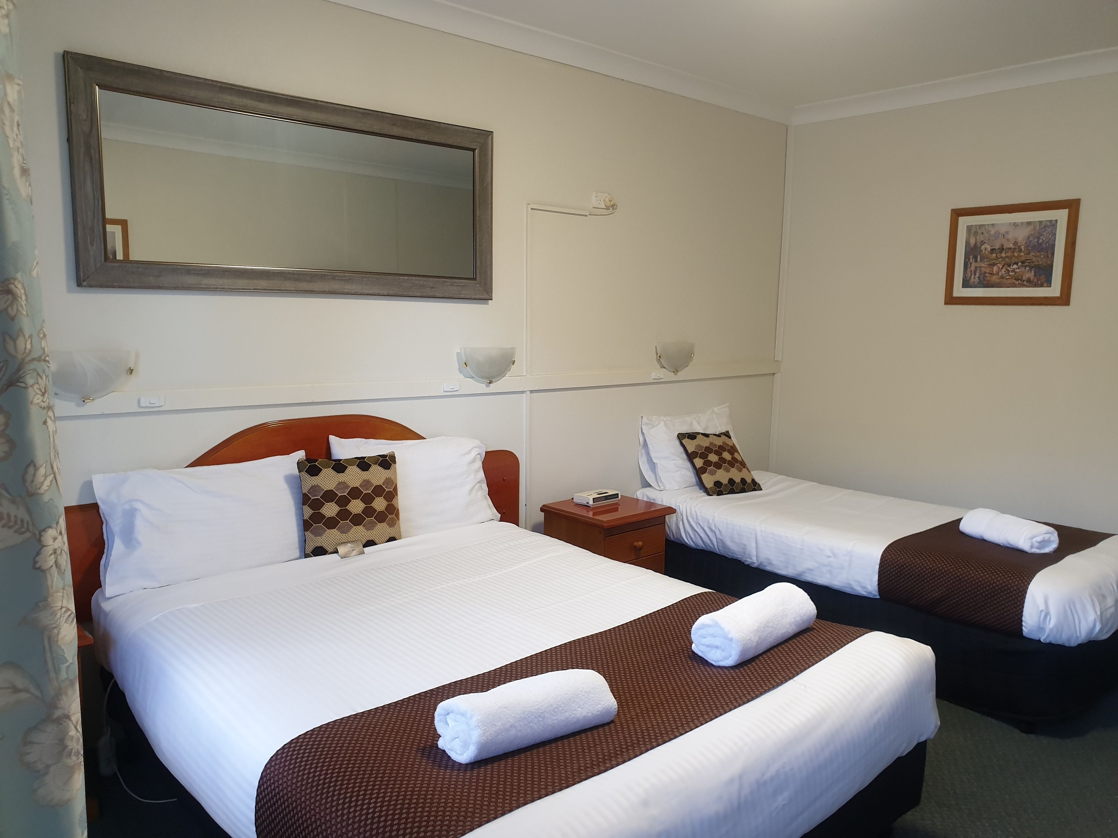 A hotel room with two beds, a large mirror, bedside lamps, and a painting on the wall.