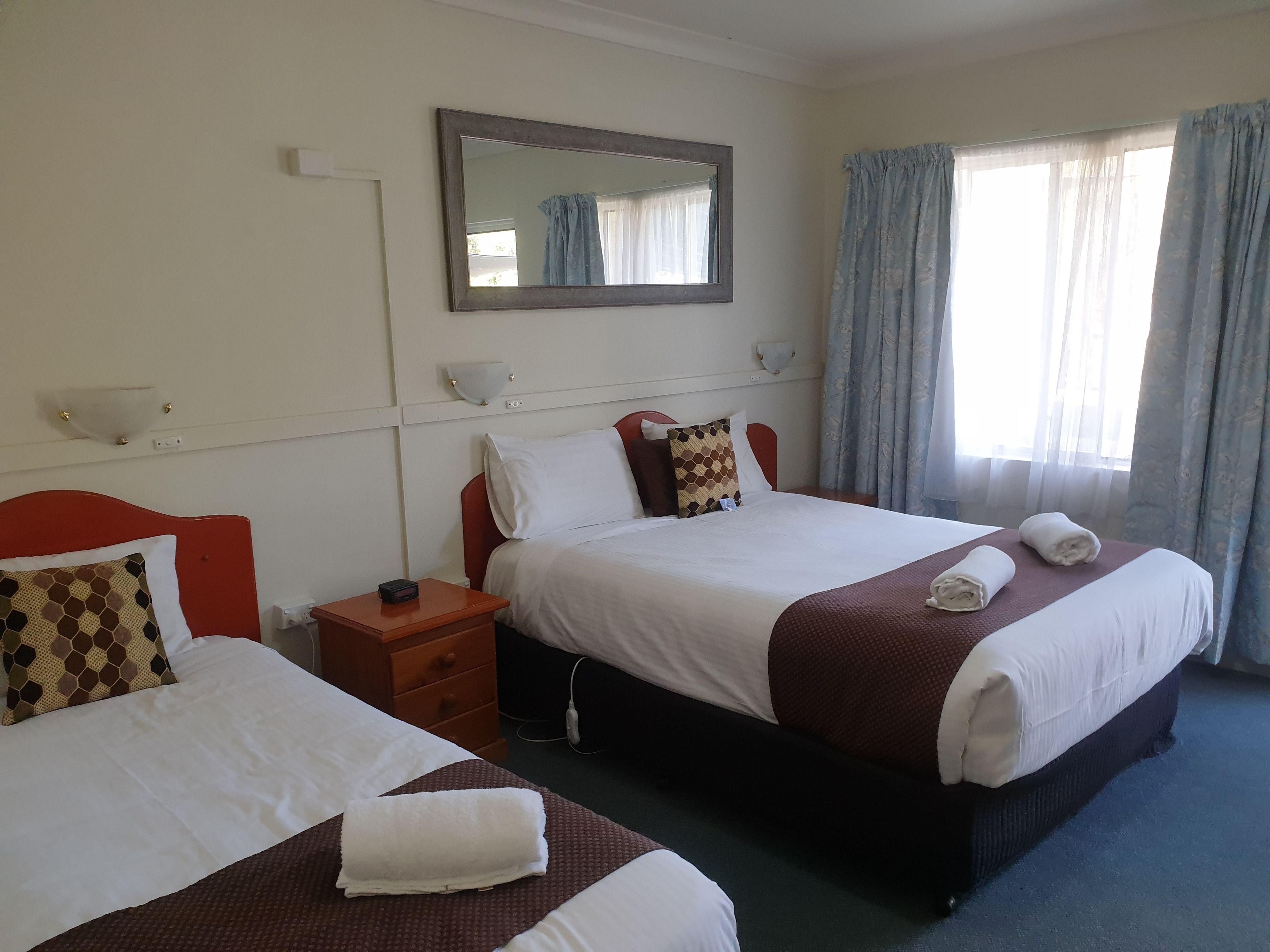 A hotel room with two beds, a nightstand, a mirror, and a window with curtains.