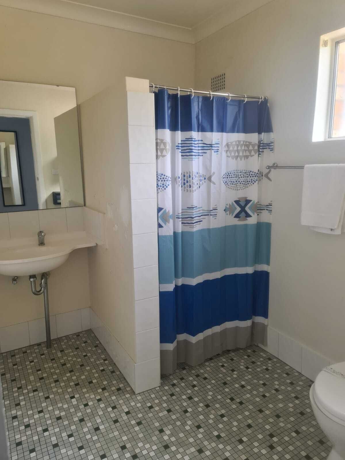 A bathroom with a tiled floor, a sink, a toilet, and a shower curtain with a fish pattern.