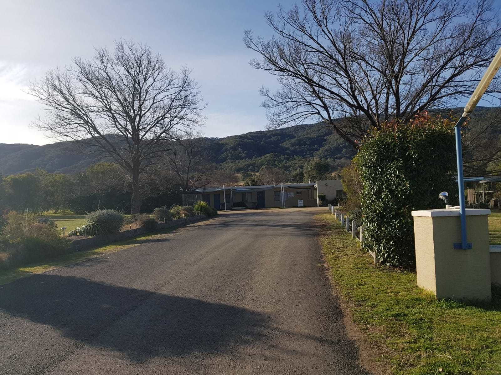 A rural road leading to a building with a covered entrance, surrounded by trees and hills.