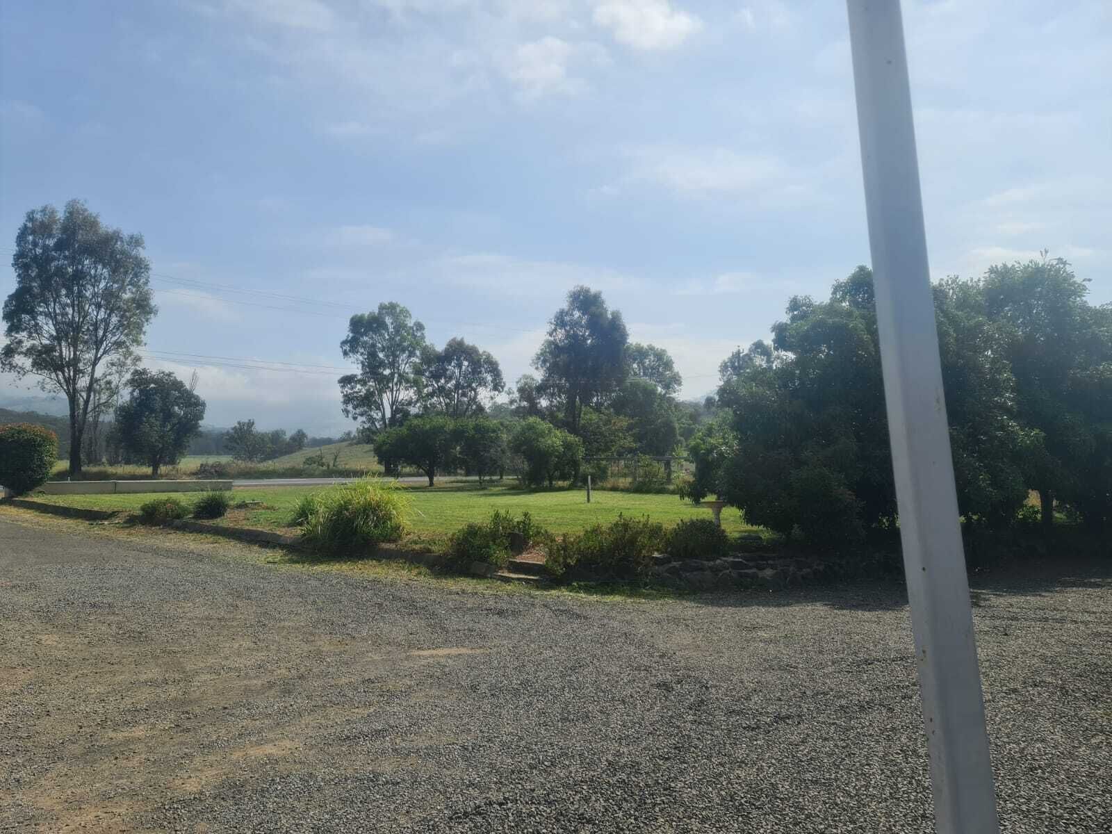 A gravel driveway leading to a grassy area with trees and a stone wall.