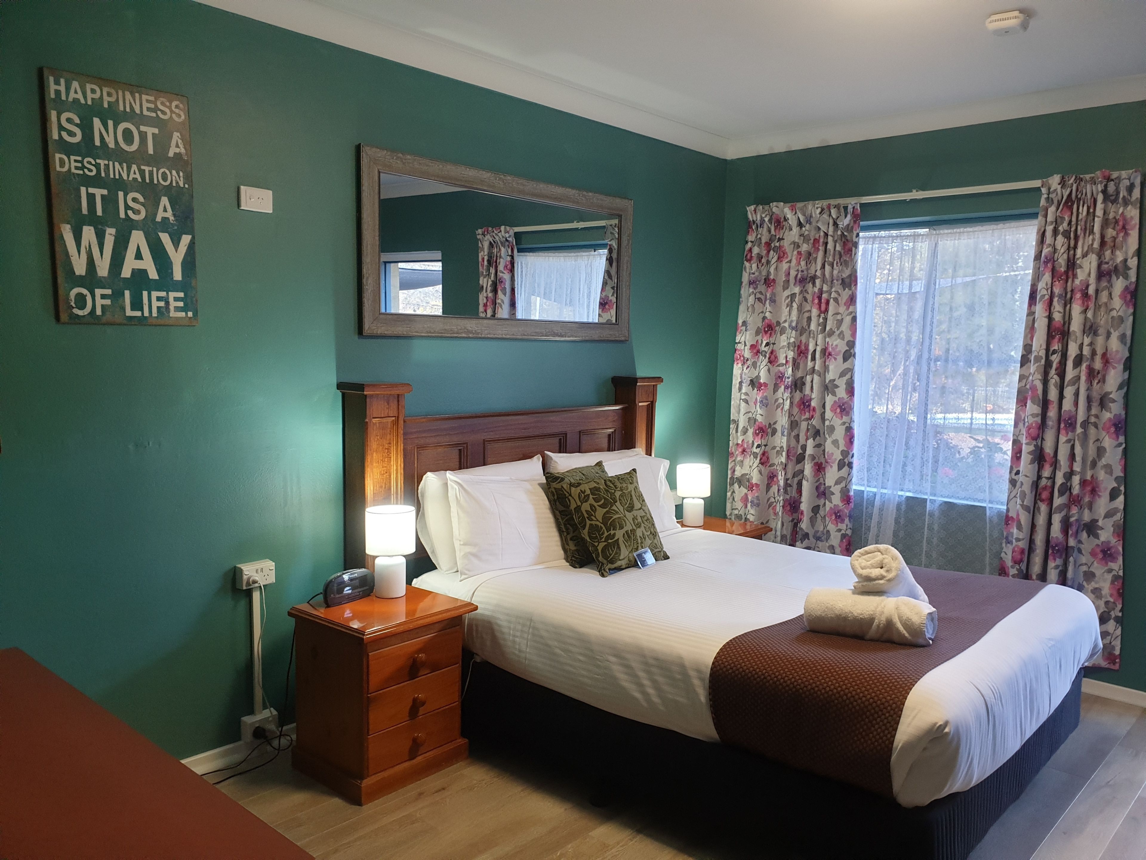 A neatly made bed with a brown blanket, two bedside lamps, and a floral curtain.