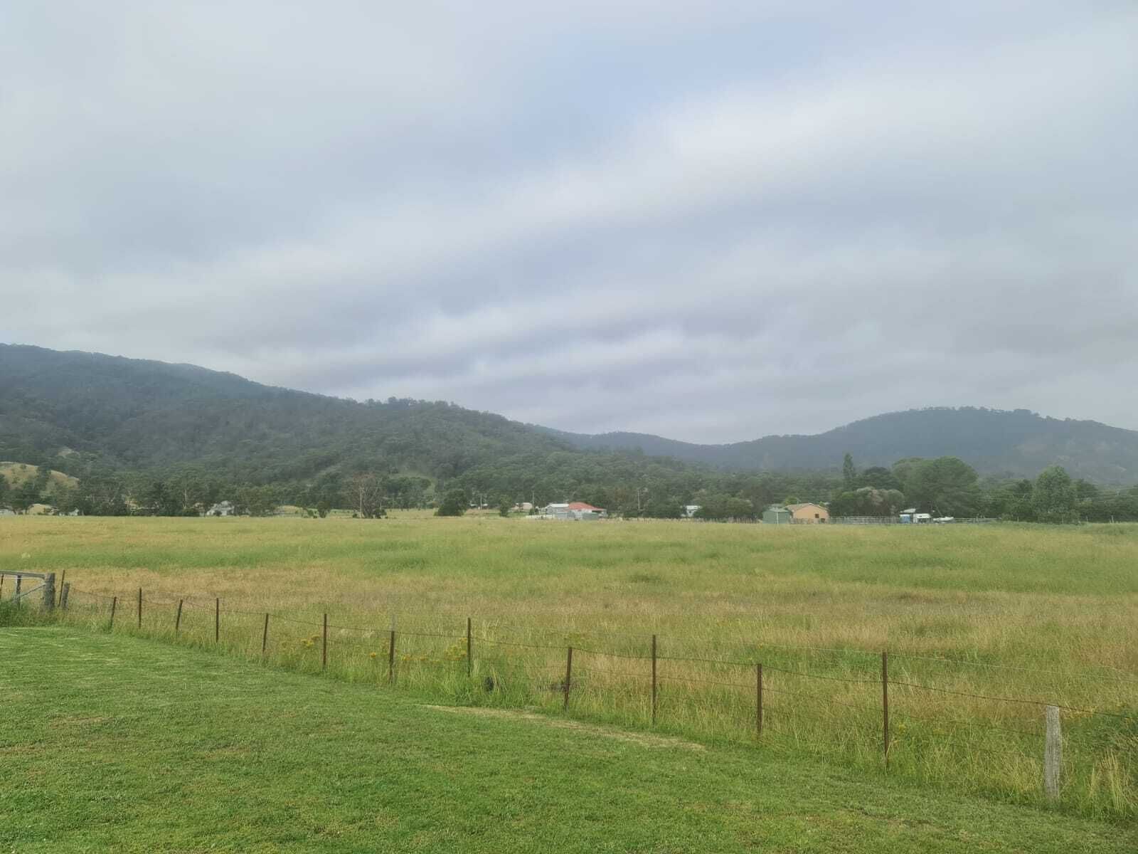A rural landscape with a field, a fence, and distant hills.