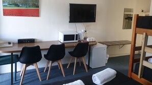 A hotel room with a desk, chairs, a TV, a microwave, a small fridge, a painting, and a bunk bed. - Valley View Motel (Murrurundi)