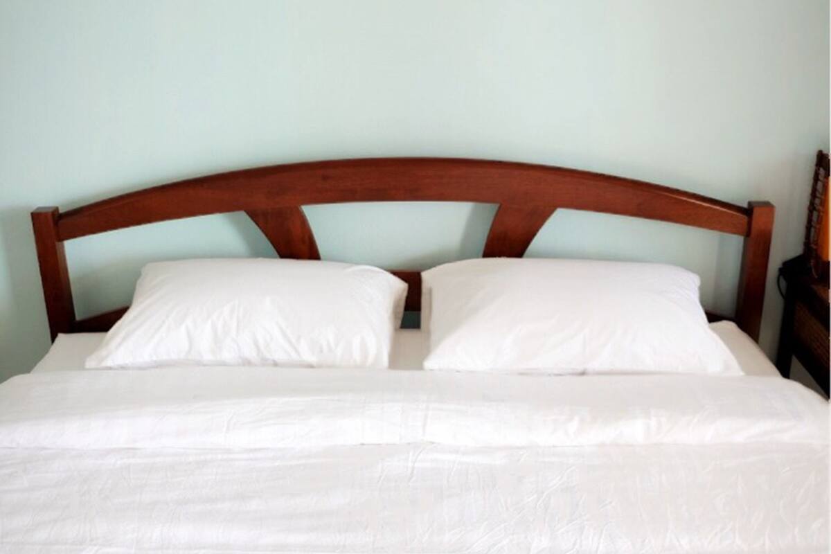 A neatly made bed with a wooden headboard, white linens, and a single pillow.