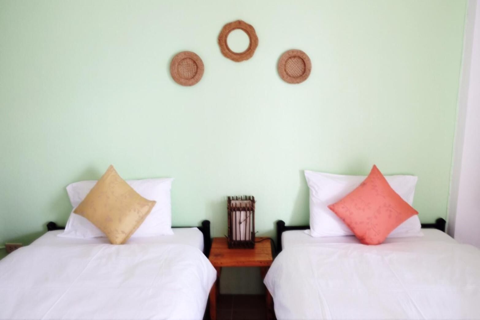 A room with two beds, each with a pillow and a small wooden nightstand between them.