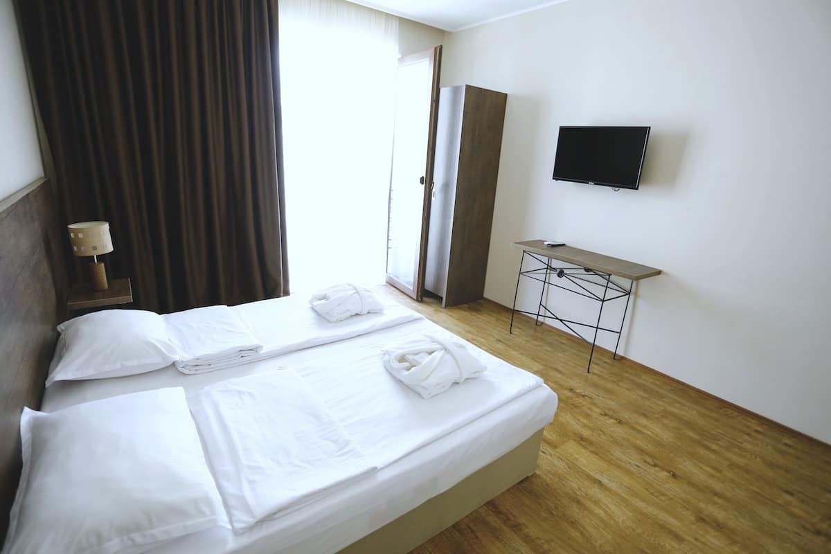 A hotel room with a bed, a desk, a TV, and a window with curtains.