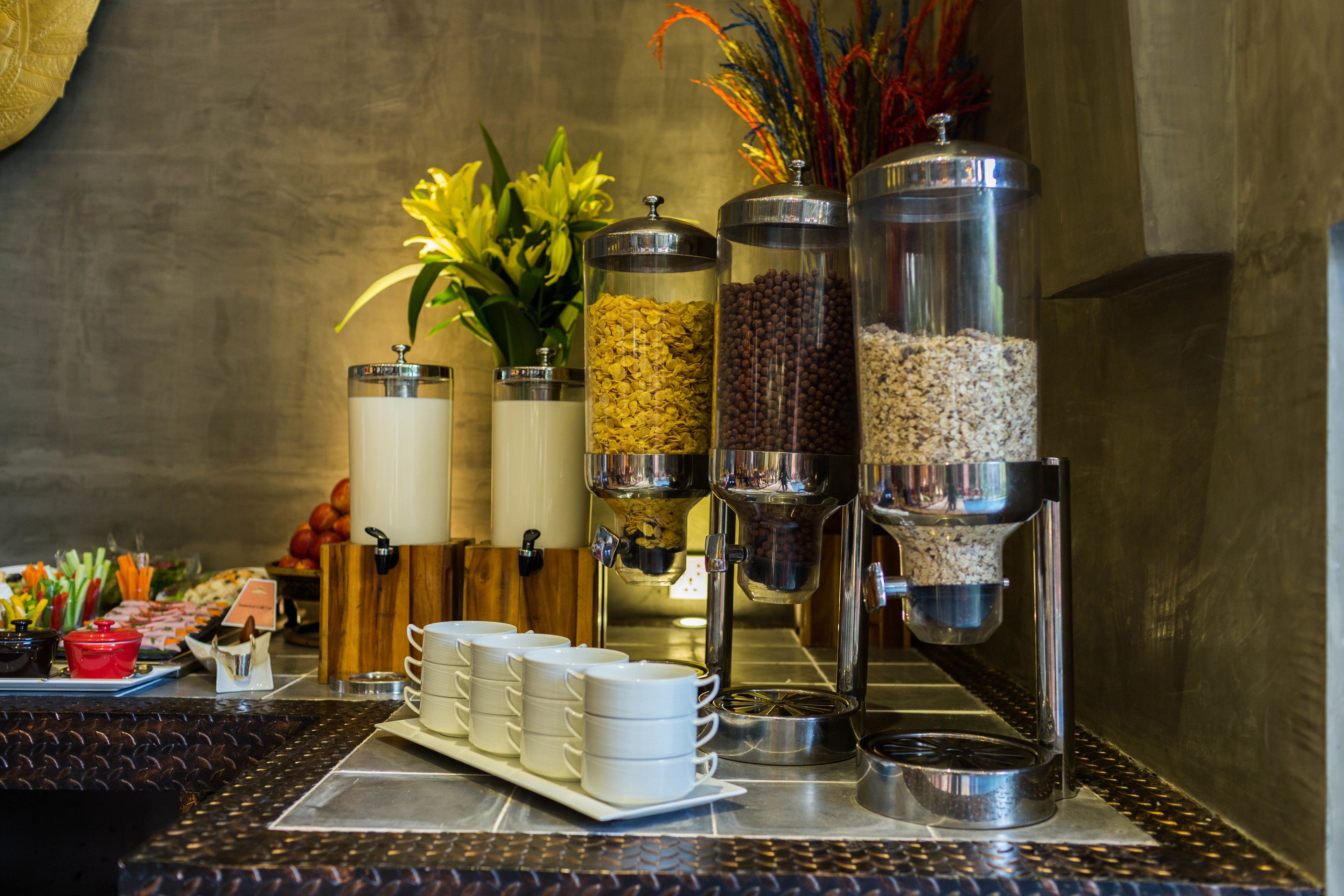 Een buffetopstelling met diverse voedselcontainers, een koffieapparaat en een bloemenarrangement.