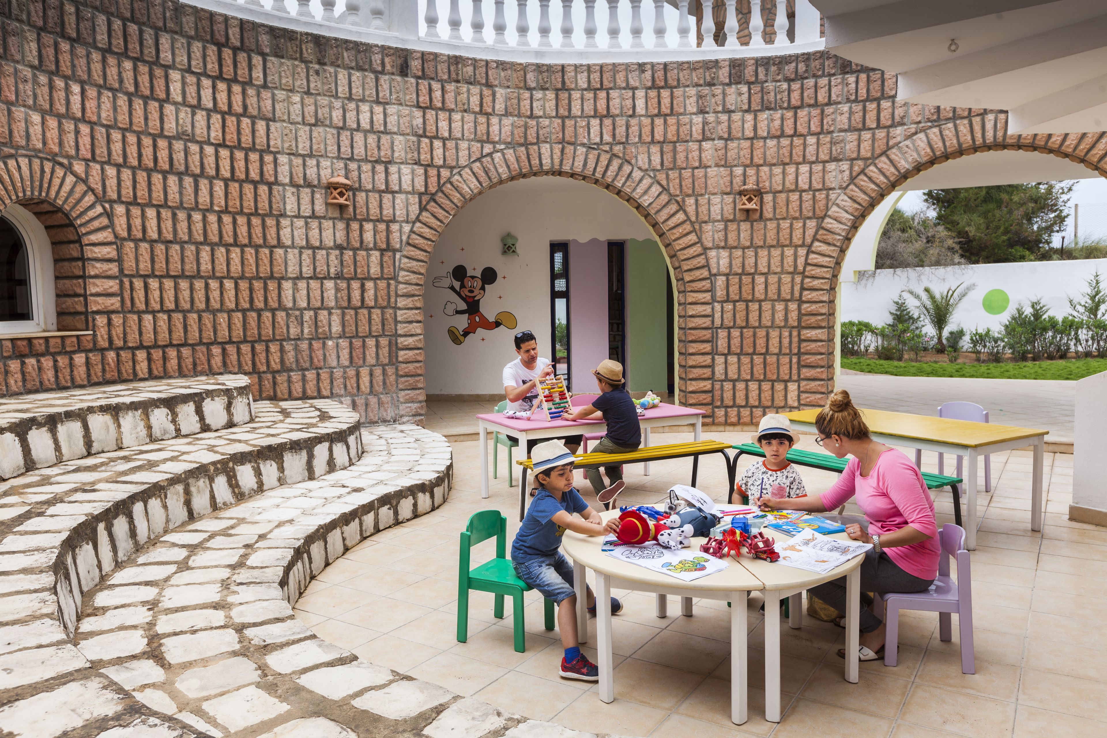 Un patio con paredes de ladrillo, mobiliario exterior y niños jugando.