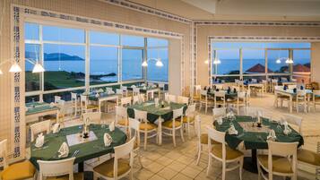 Un restaurante con varias mesas dispuestas para comer, amplias ventanas con vista al mar y decoración de pared con diseño.