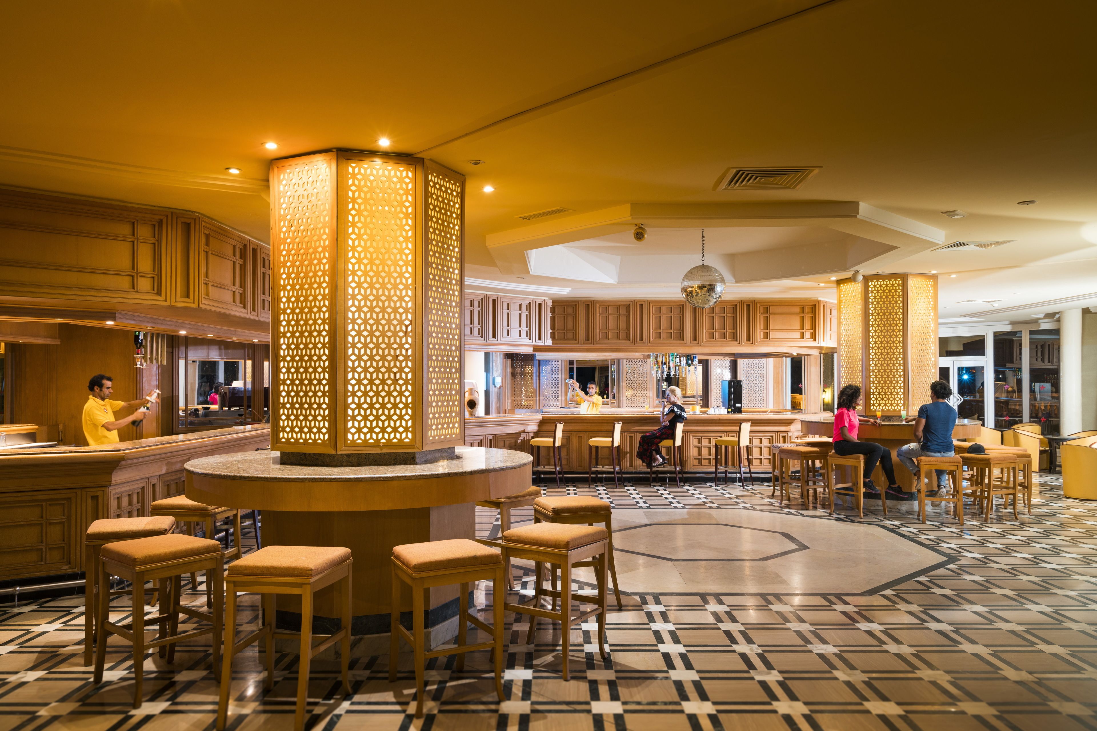 A hotel lobby with a central bar area, multiple seating options, and a patterned floor.