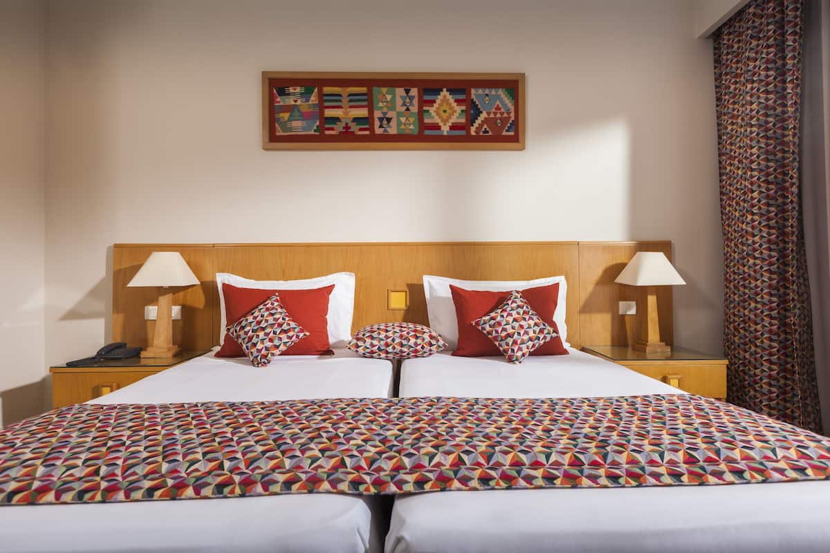 Un lit double avec une couvre-lit à motifs géométriques, deux oreillers rouges et une œuvre d’art accrochée au mur au-dessus.
