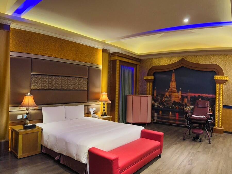 A hotel room with a large bed, a red bench, a desk, and a chair.