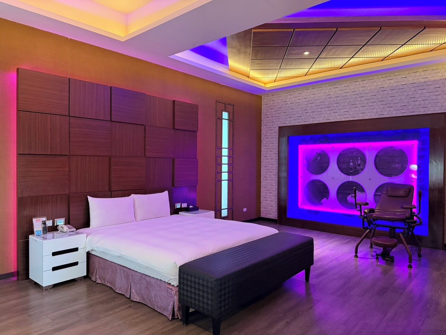 A modern bedroom with a large bed, bedside tables, a bench, and a massage chair.