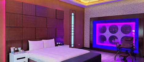 A modern bedroom with a large bed, bedside tables, a bench, and a massage chair.