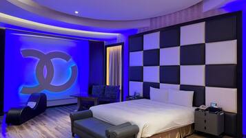Une chambre moderne avec un grand lit, un coin salon, une table de chevet et un mur orné d’un grand logo.