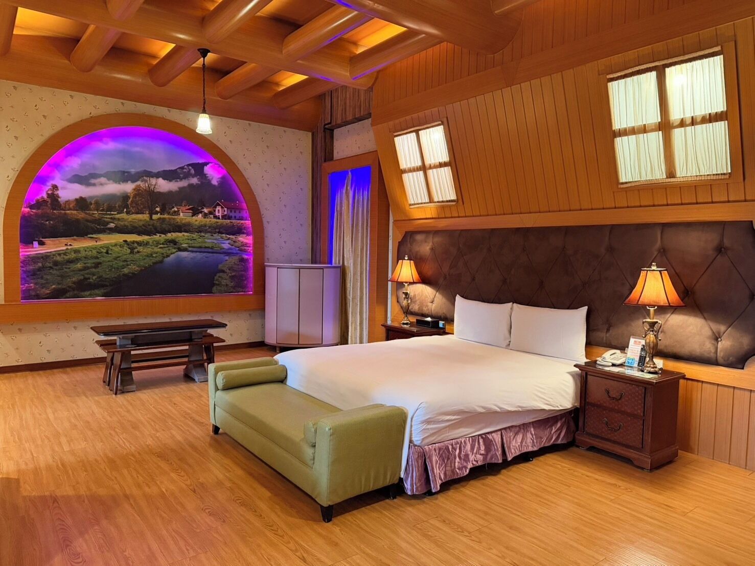 Een slaapkamer met een groot bed, een bankje, een nachtkastje en een aan de muur bevestigde televisie.