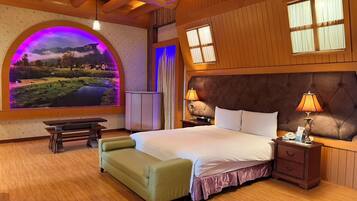 Een slaapkamer met een groot bed, een bankje, een nachtkastje en een aan de muur bevestigde televisie.