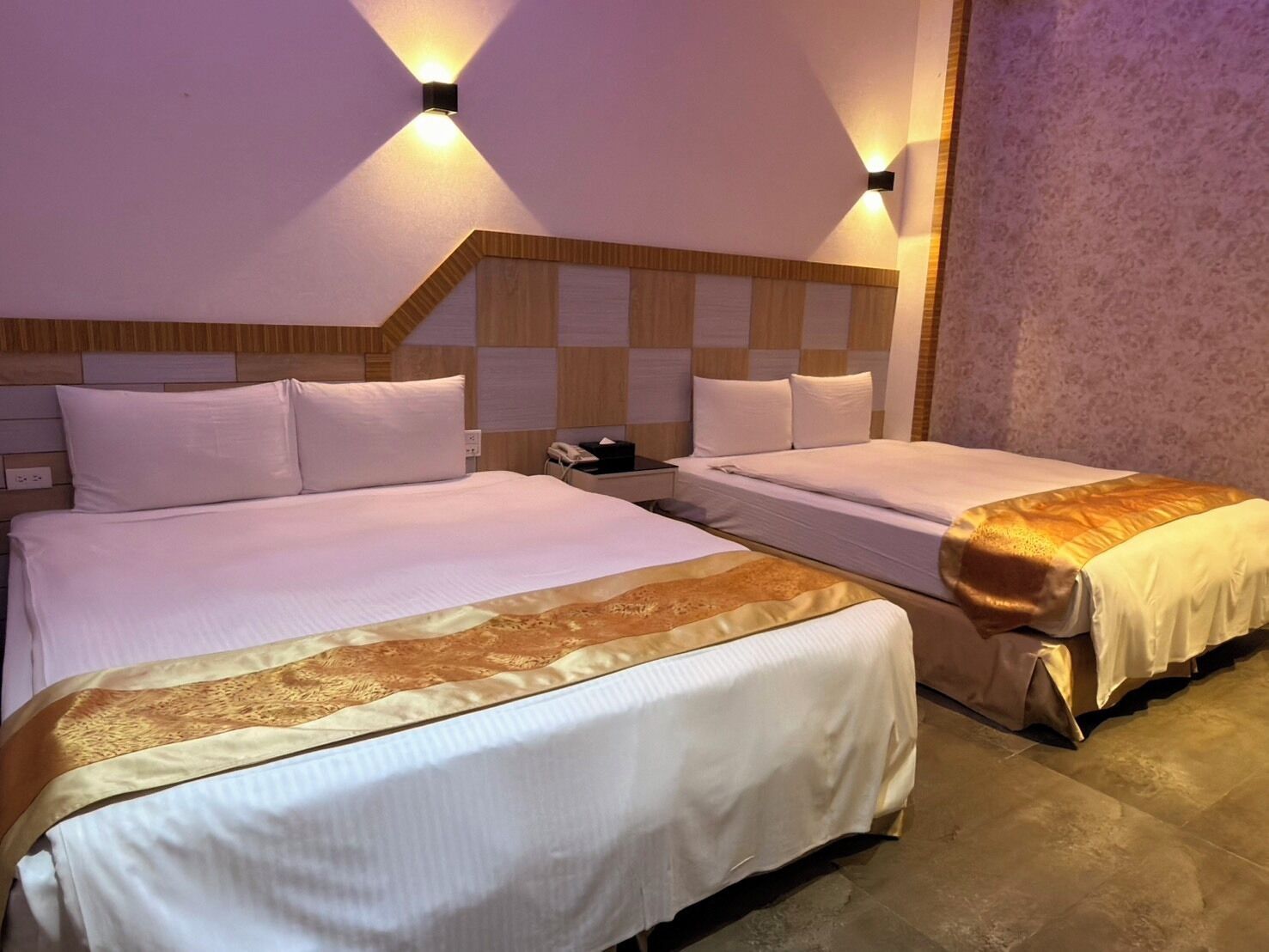 Habitación de hotel con dos camas, cabecero de madera y dos lámparas fijadas a la pared.