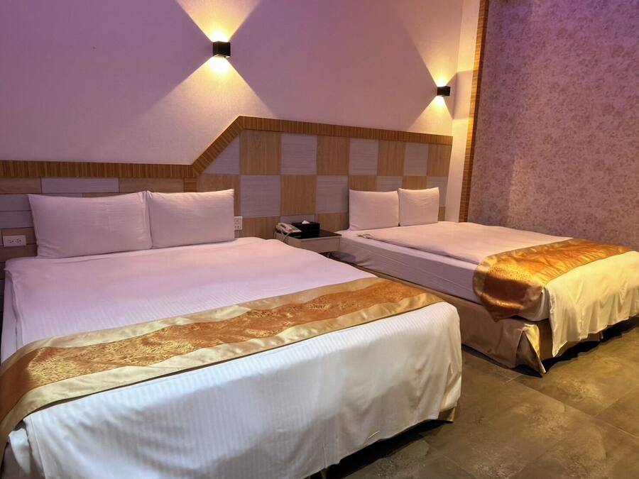 Habitación de hotel con dos camas, cabecero de madera y dos lámparas fijadas a la pared.