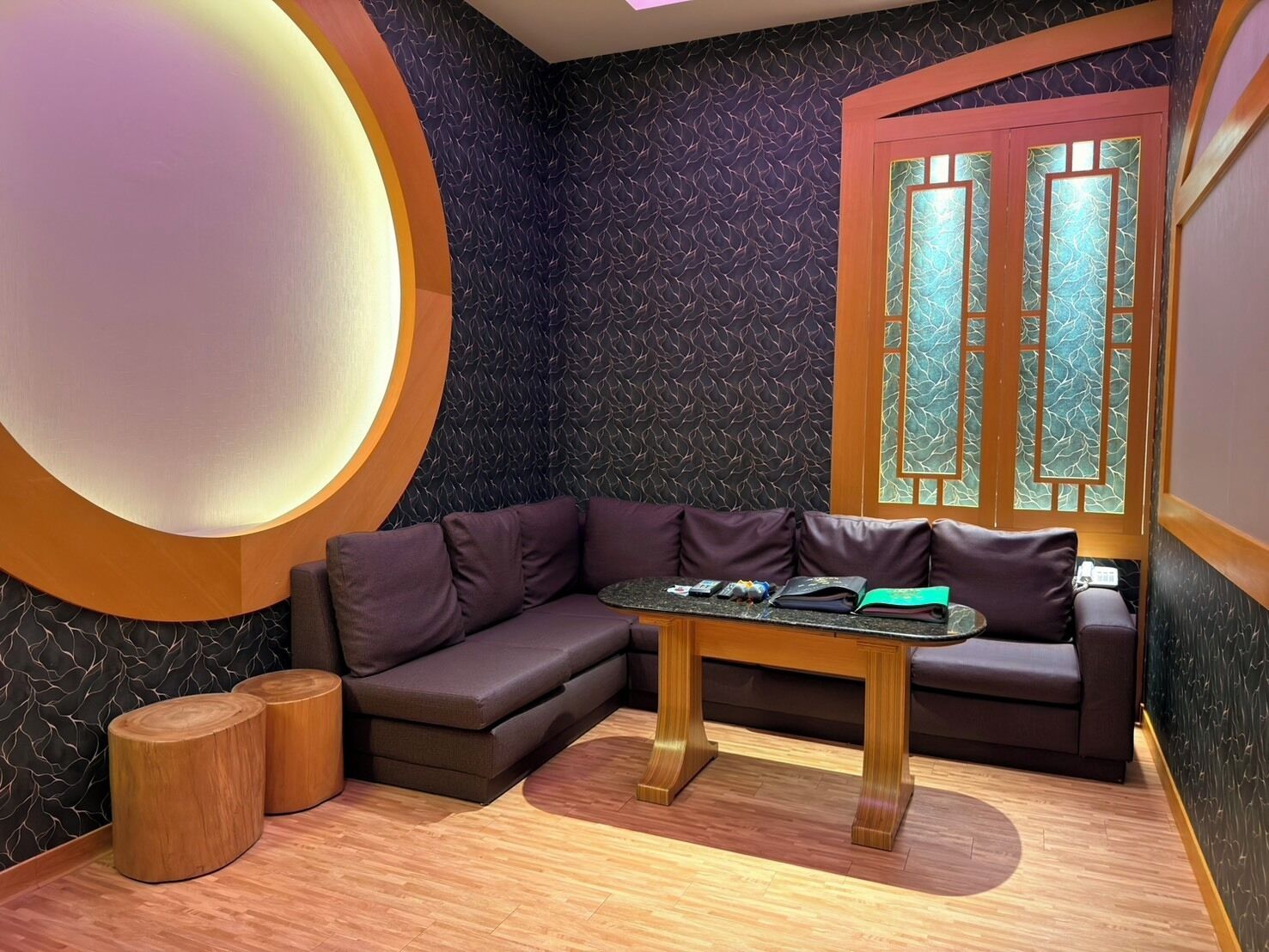 A modern room with a dark patterned wall, a round light fixture, a wooden table with a book, and a dark-colored sofa.