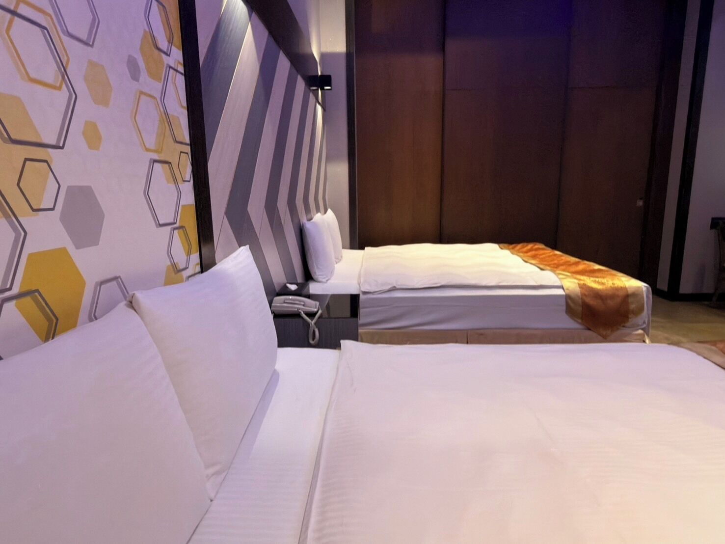 Hotellihuone, jossa on kaksi sänkyä, moderni, geometrisesti kuvioitu seinä ja puuovi.