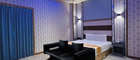 A modern hotel room with a bed, a black sofa, a small round table, and patterned wallpaper.