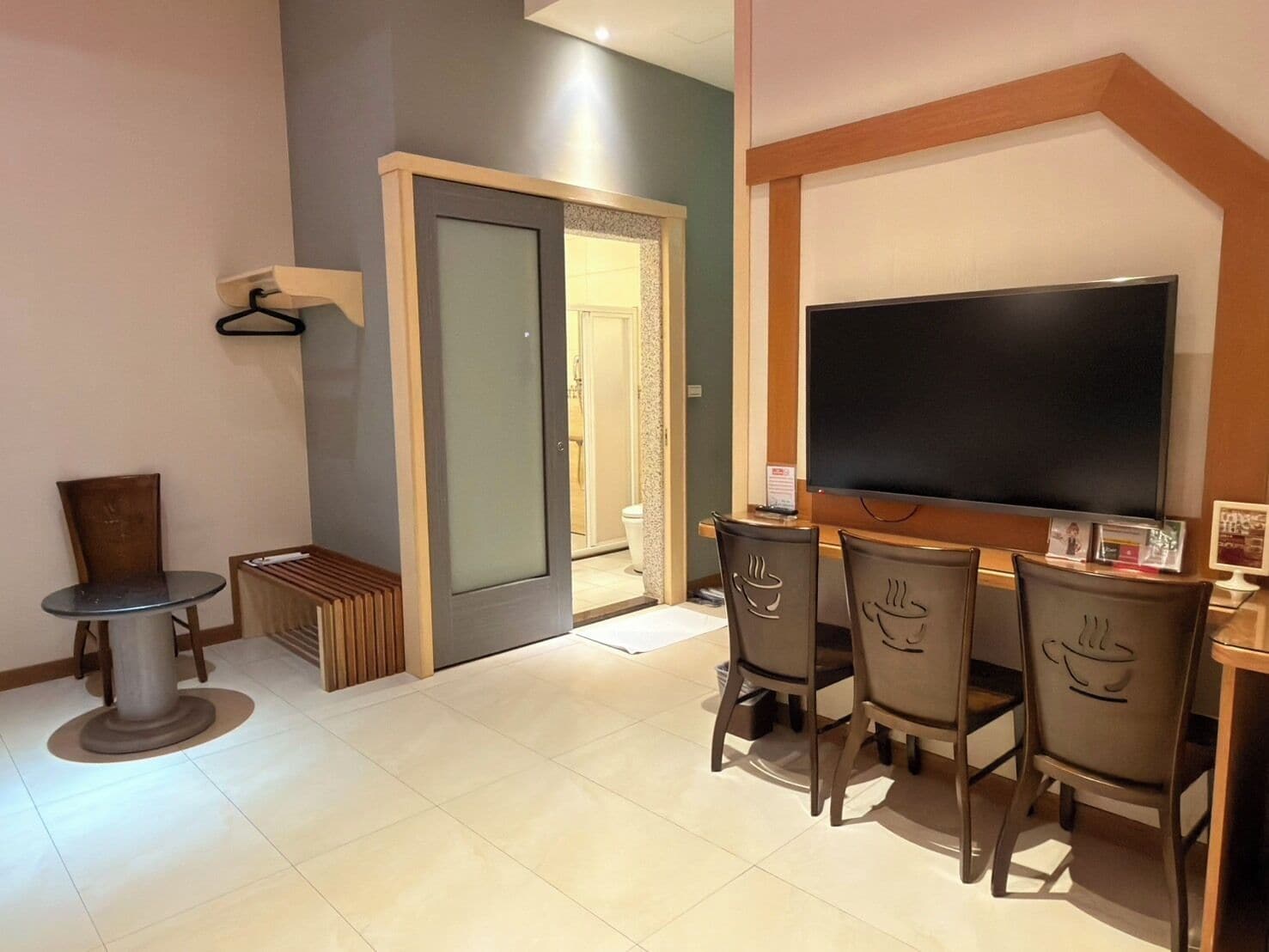A hotel room with a TV, a small table, a bench, and four chairs with a coffee cup design.
