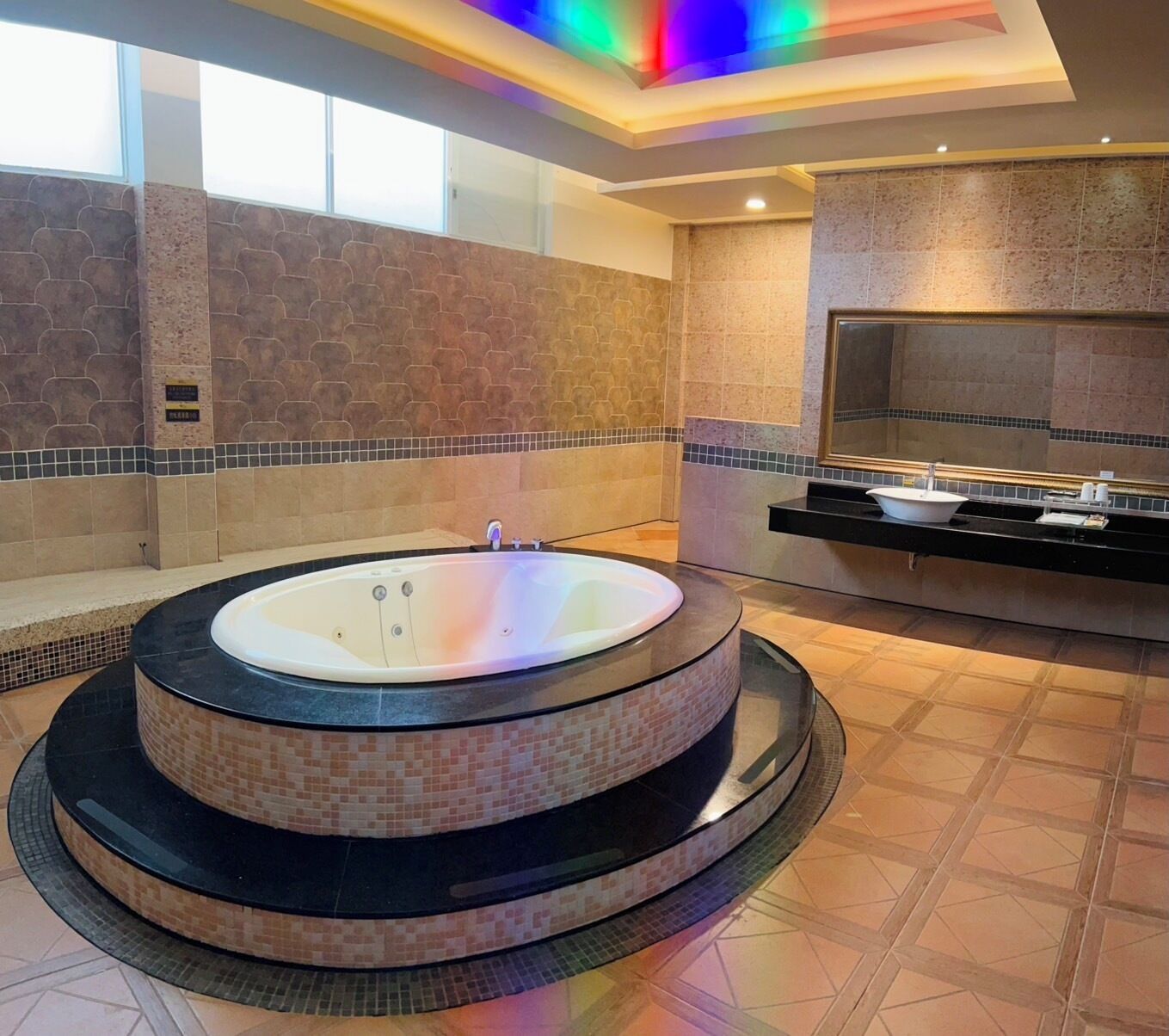 A modern bathroom with a circular hot tub, a large mirror, and a tiled floor.