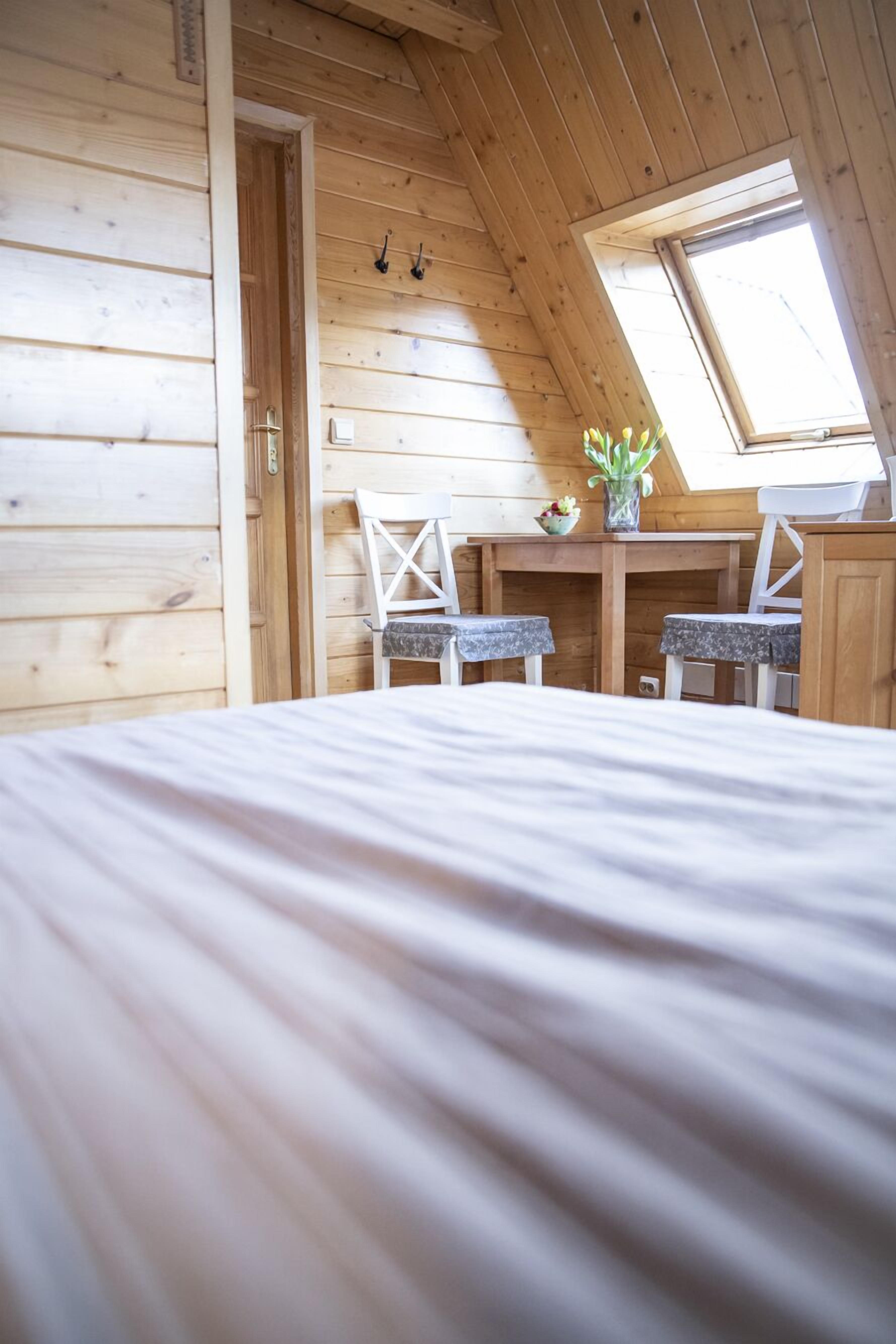 A cozy room with a sloped ceiling, wooden walls, a bed, two chairs, a small table with a vase, and a window.