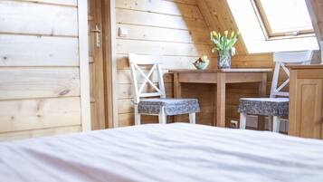 A cozy room with a sloped ceiling, wooden walls, a bed, two chairs, a small table with a vase, and a window.