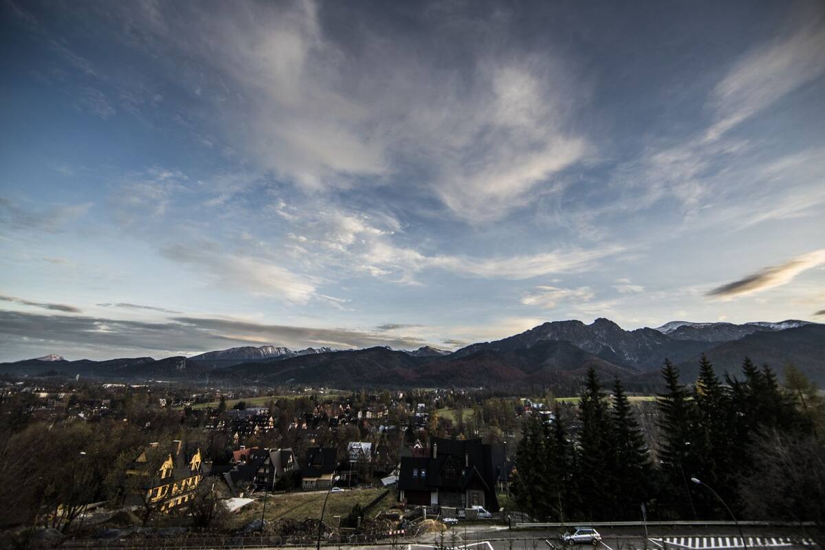 Une ville située au pied d’une montagne, avec un mélange de bâtiments résidentiels et commerciaux, une église imposante et un ciel dégagé.