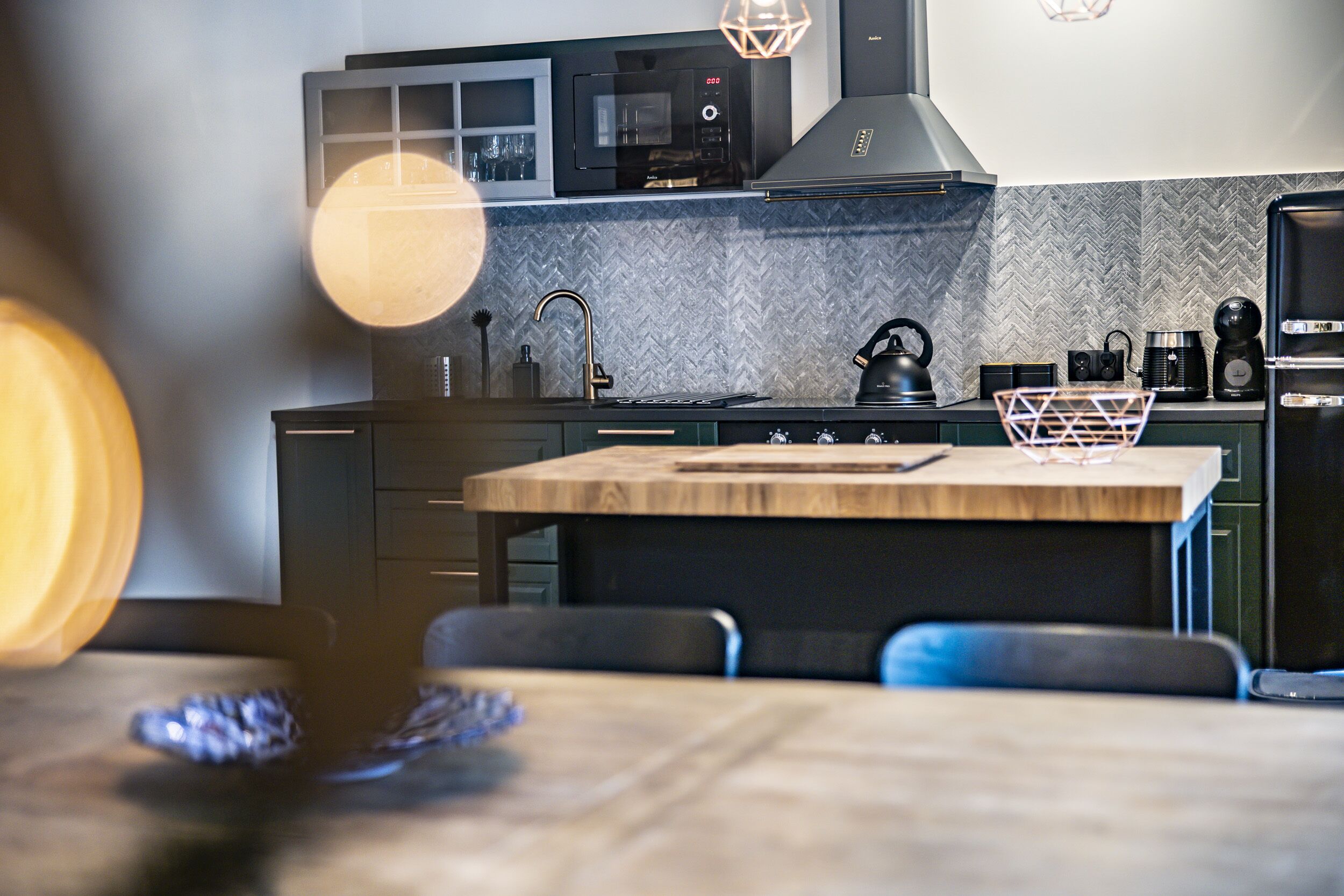 A modern kitchen with a microwave, stove, and sink. There is a wooden table with chairs and a decorative basket.