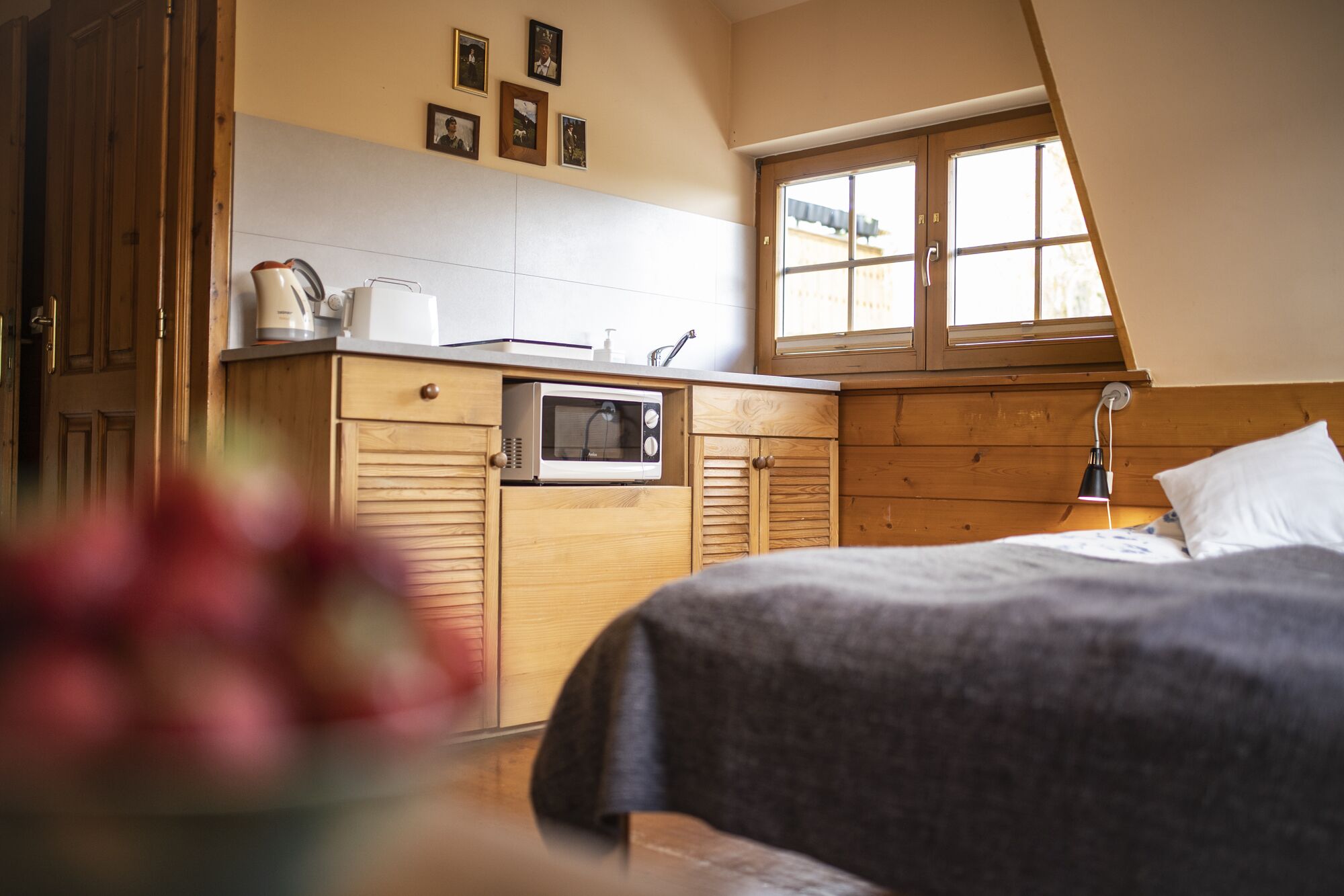 A bedroom with a bed, a wooden wardrobe, a microwave, and a window.