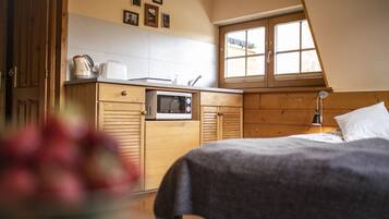 A bedroom with a bed, a wooden wardrobe, a microwave, and a window.