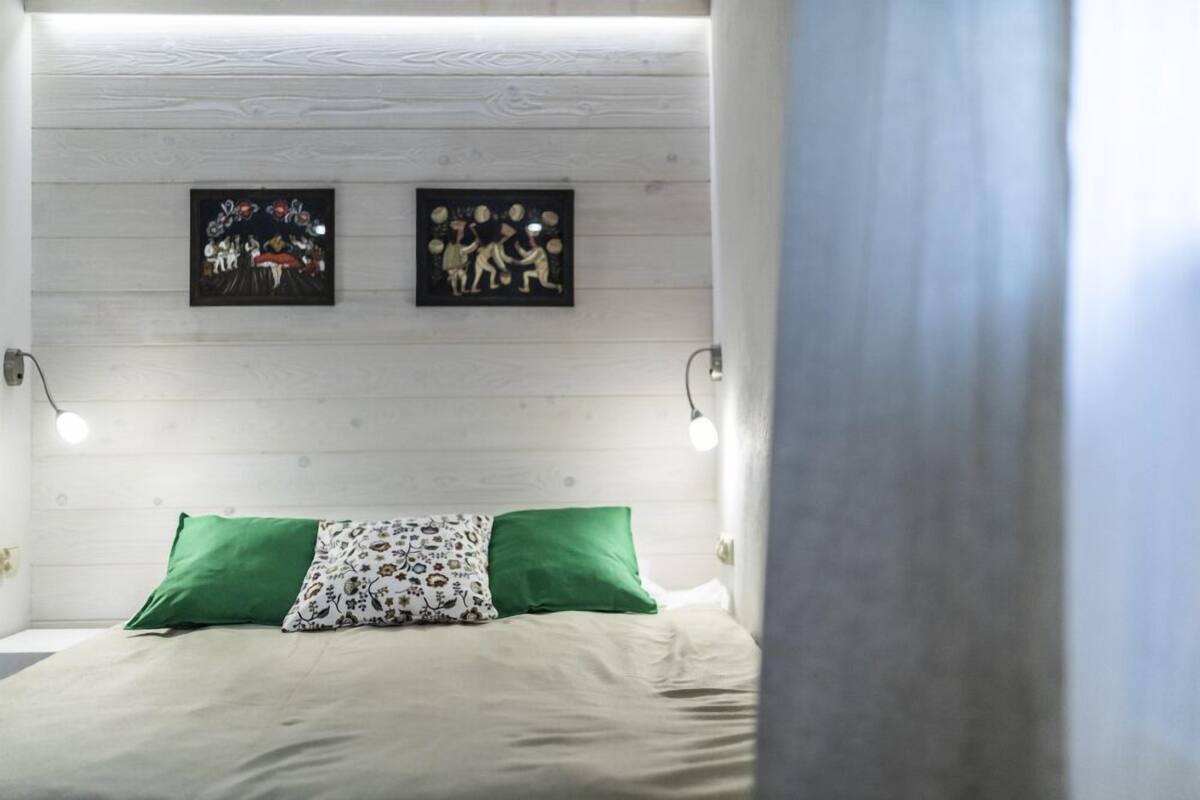 Un lit avec des oreillers verts et à motifs, deux œuvres d’art accrochées au mur et des lampes de chevet.