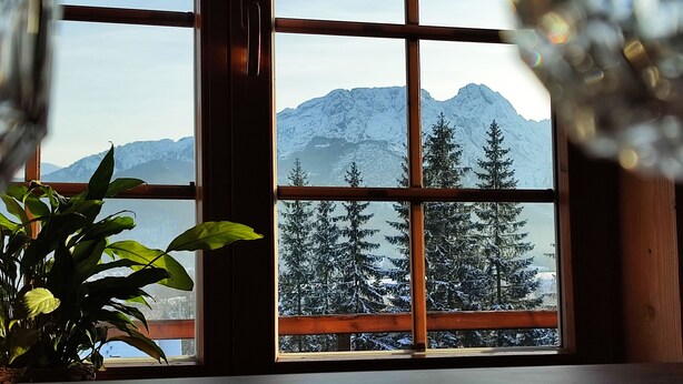 Quarto com uma grande janela que oferece vista para montanhas cobertas de neve e árvores perenes.