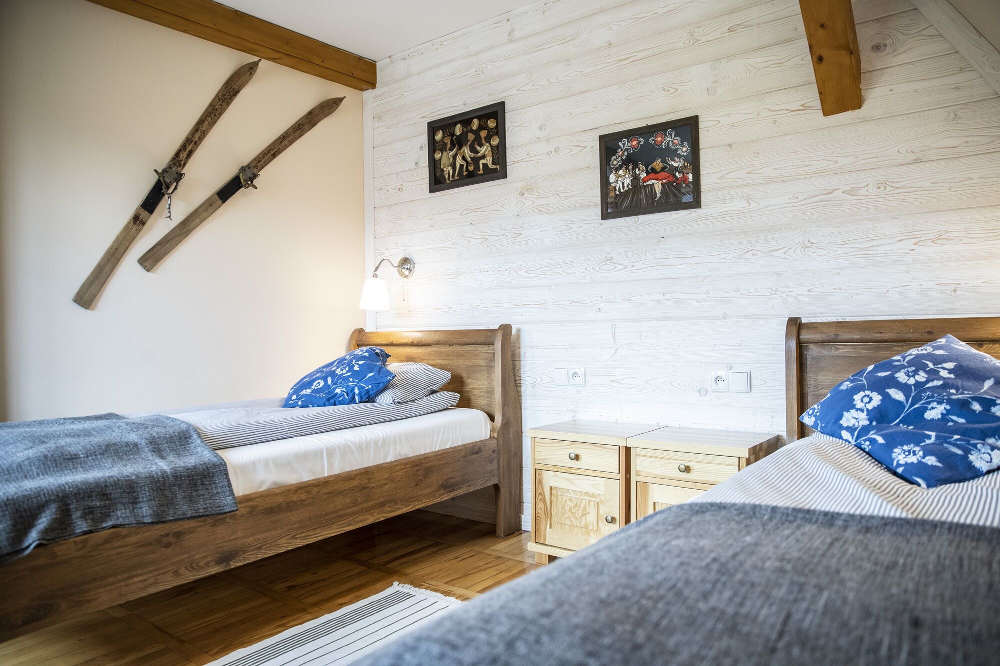 Un dormitorio con dos camas de madera, una mesita de noche y una lámpara fijada a la pared.