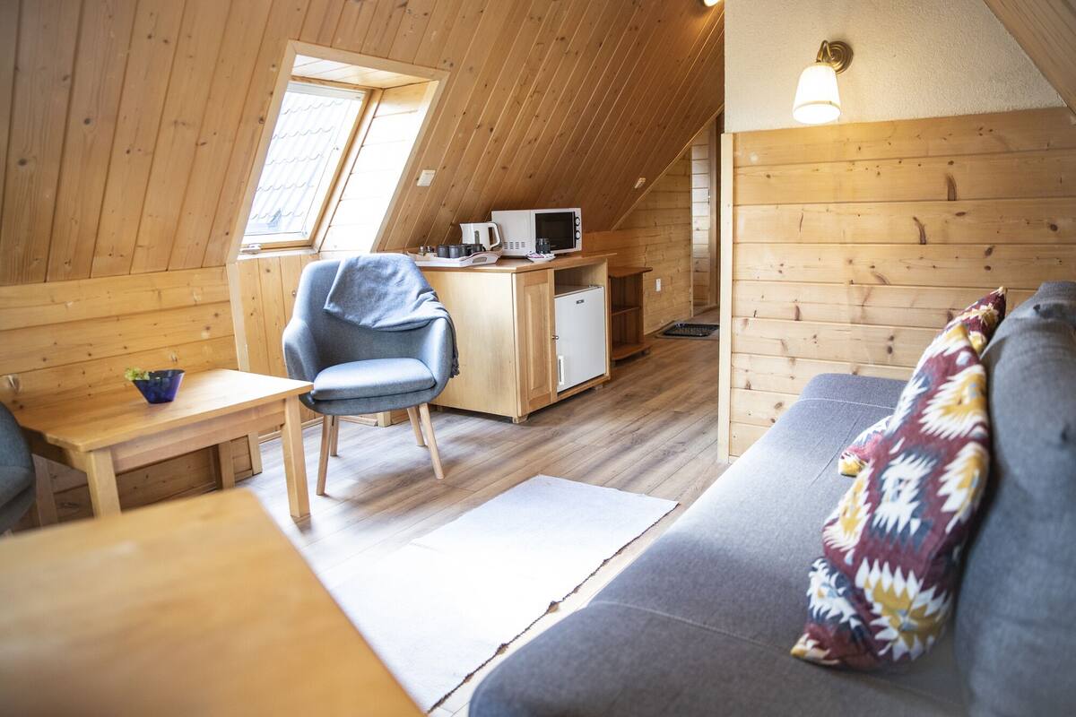 Un intérieur de chalet chaleureux, avec un revêtement en bois, un coin cuisine, un canapé et un espace repas.