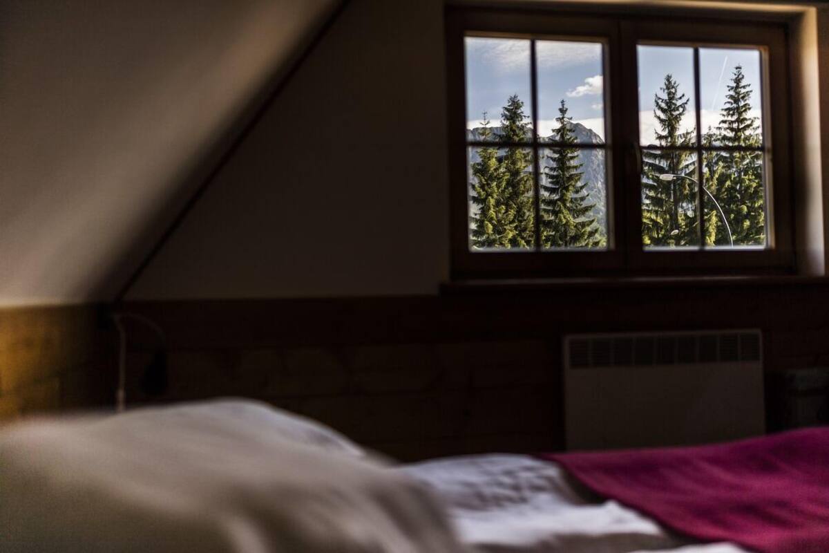 Une chambre à coucher avec un lit, une fenêtre donnant sur des arbres et des montagnes, et un plafond en pente.