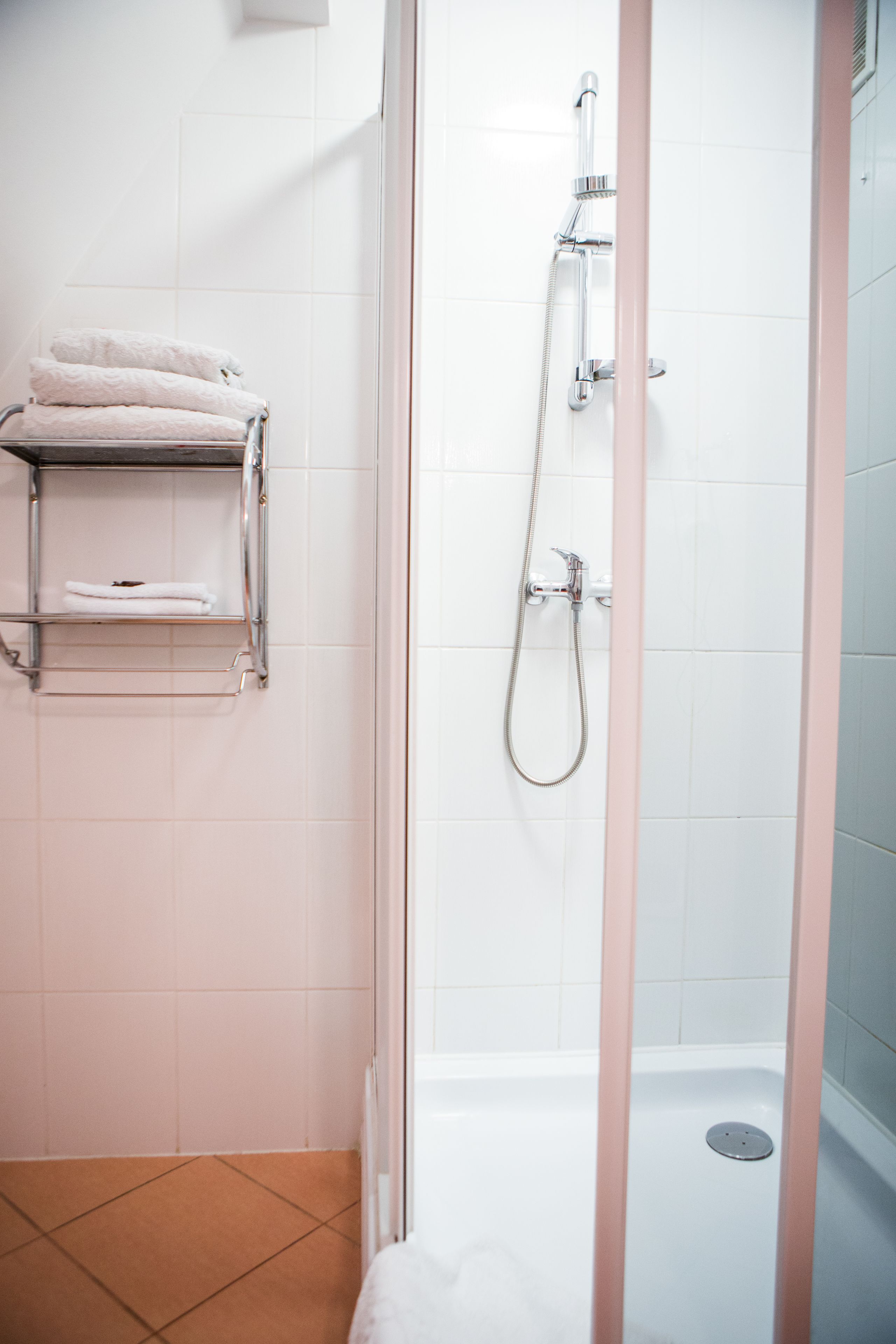 A bathroom with a glass-enclosed shower, a towel rack with folded towels, and a showerhead.