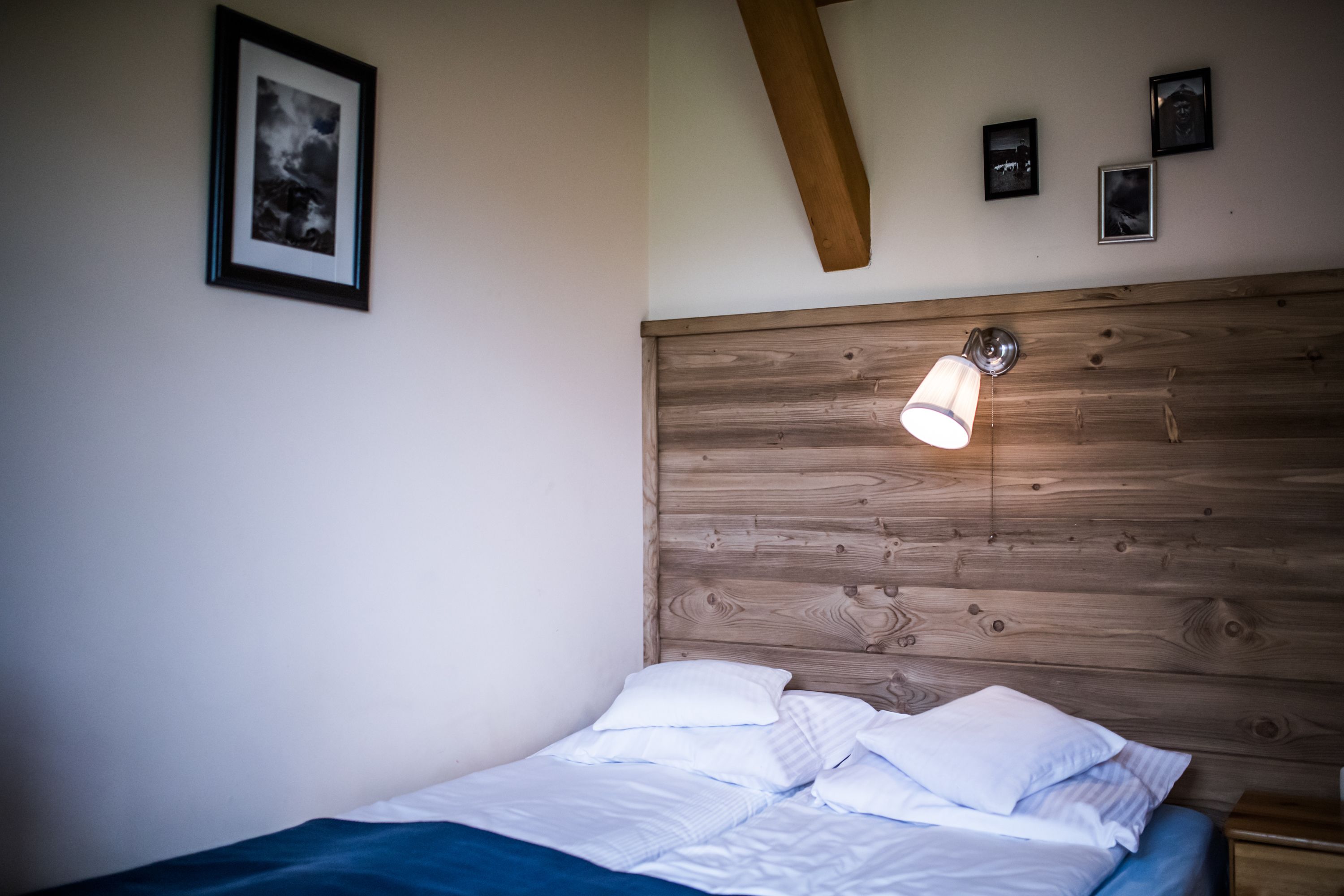 A bedroom with a wooden headboard, a bed with white bedding, and a wall-mounted light fixture.