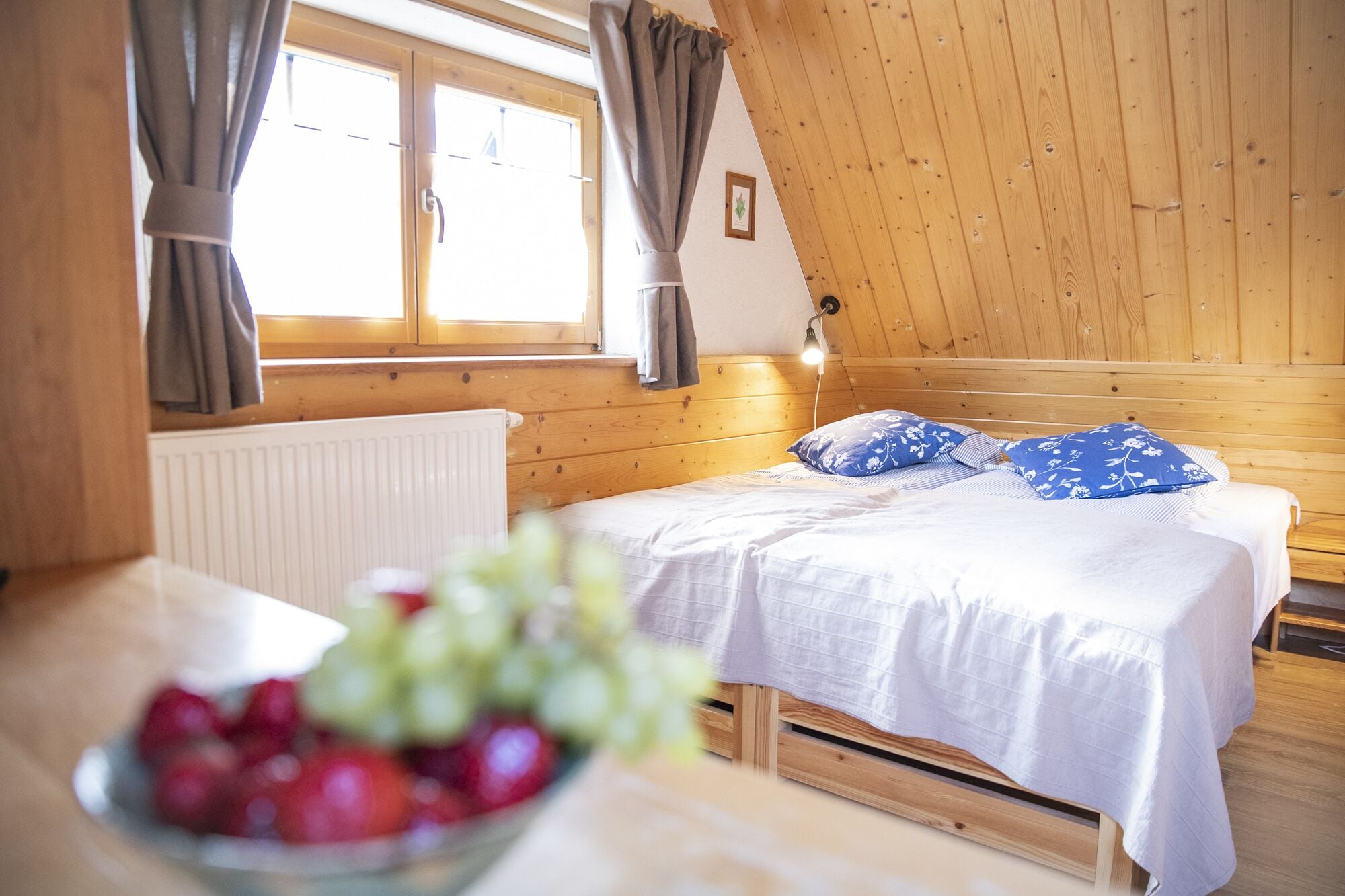 A cozy wooden room with a bed, a radiator, and a table with fruit.